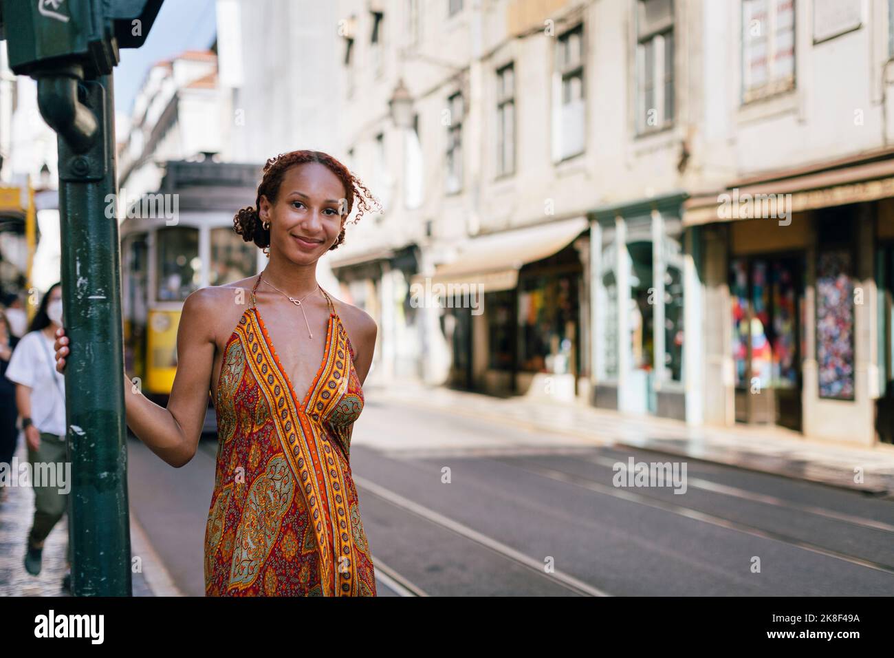 Lächelnde junge Frau, die auf dem Fußweg an der Stange steht Stockfoto