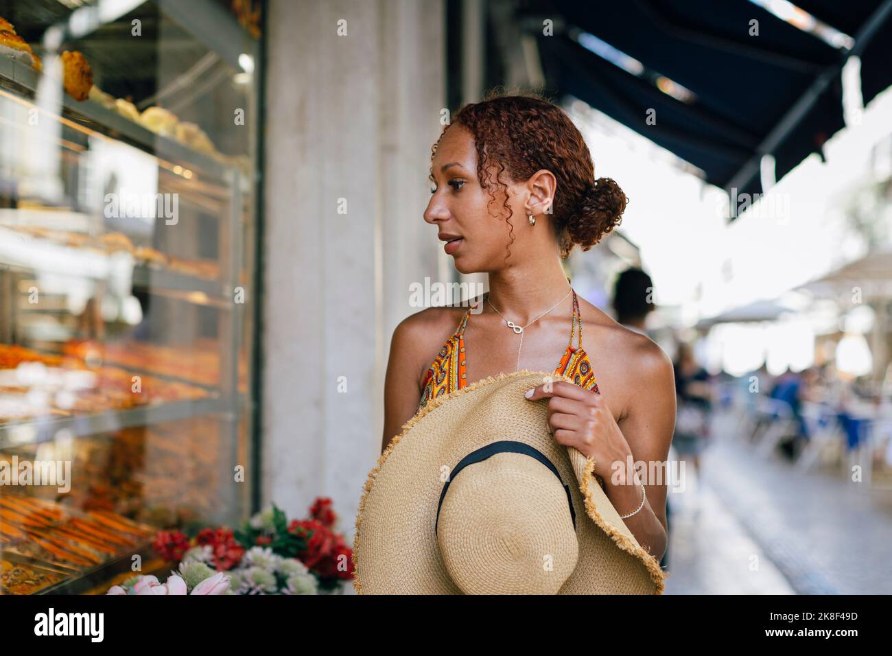 Hungrige junge Frau mit Hut, die durch das Fenster des Delikatessengeschäfts schaut Stockfoto