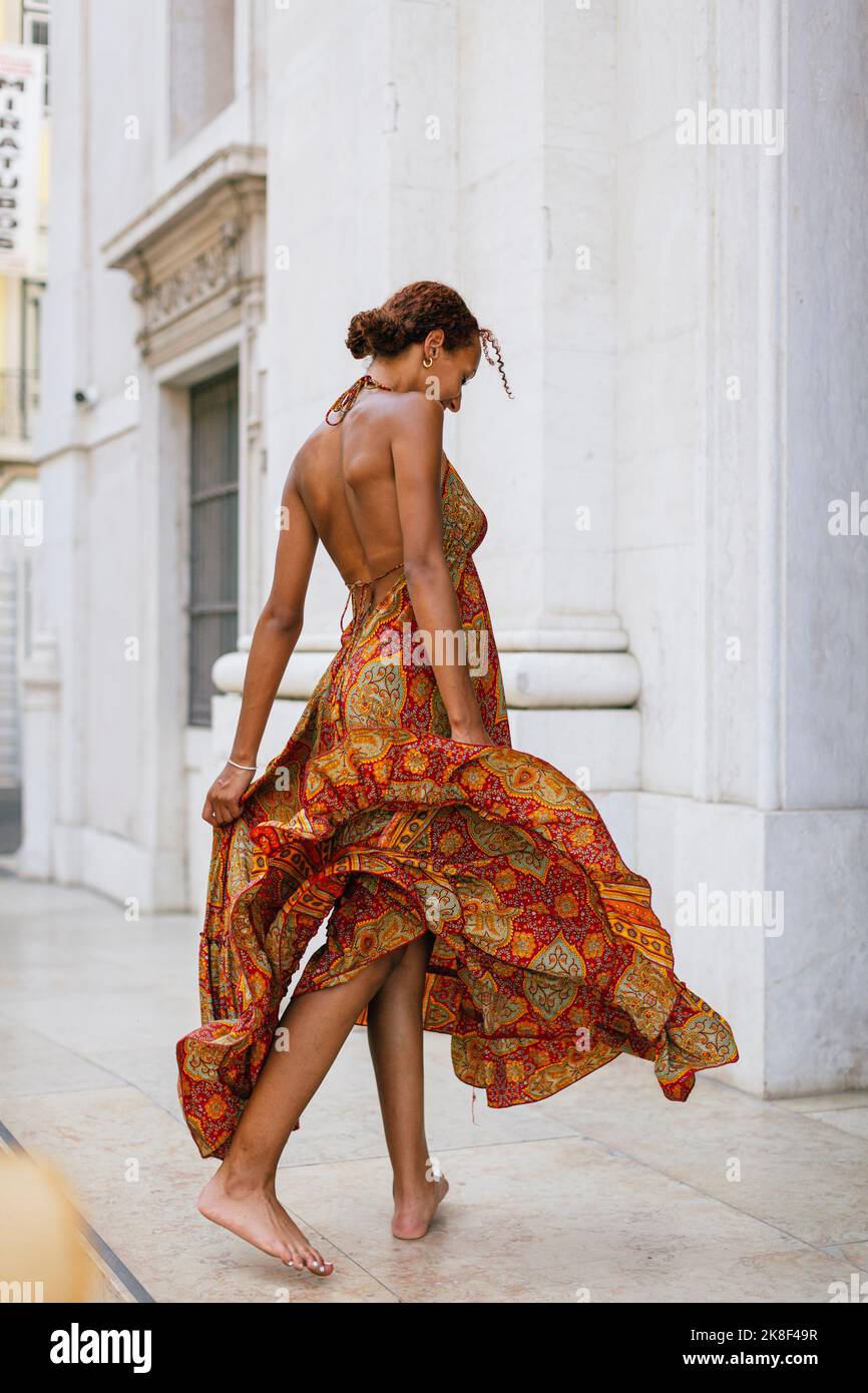 Junge Frau im Sommerkleid, die vor dem Gebäude läuft Stockfoto