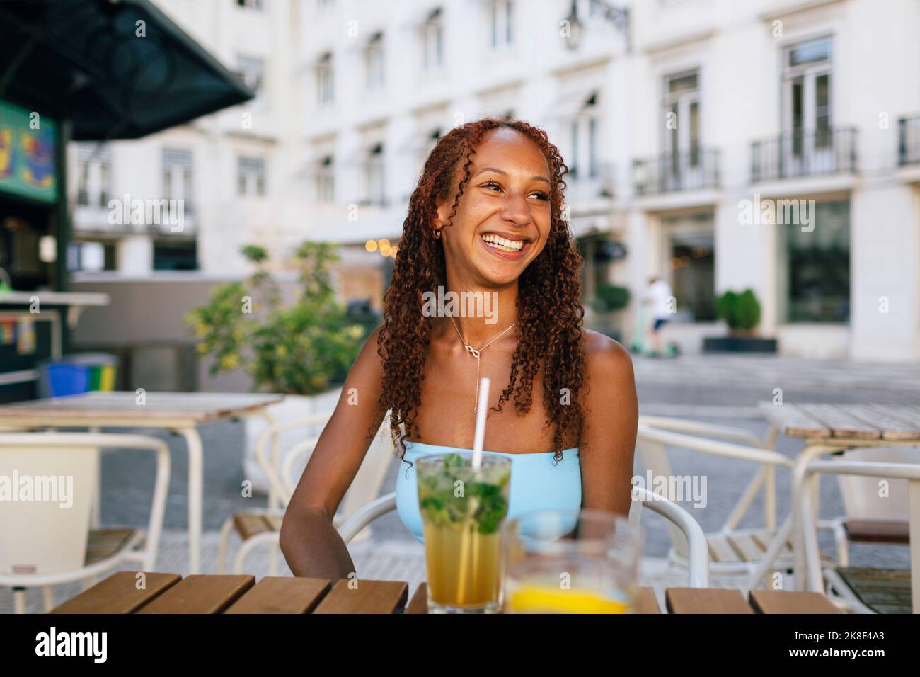 Glückliche junge Frau mit lockigen Haaren sitzt im Straßencafé Stockfoto