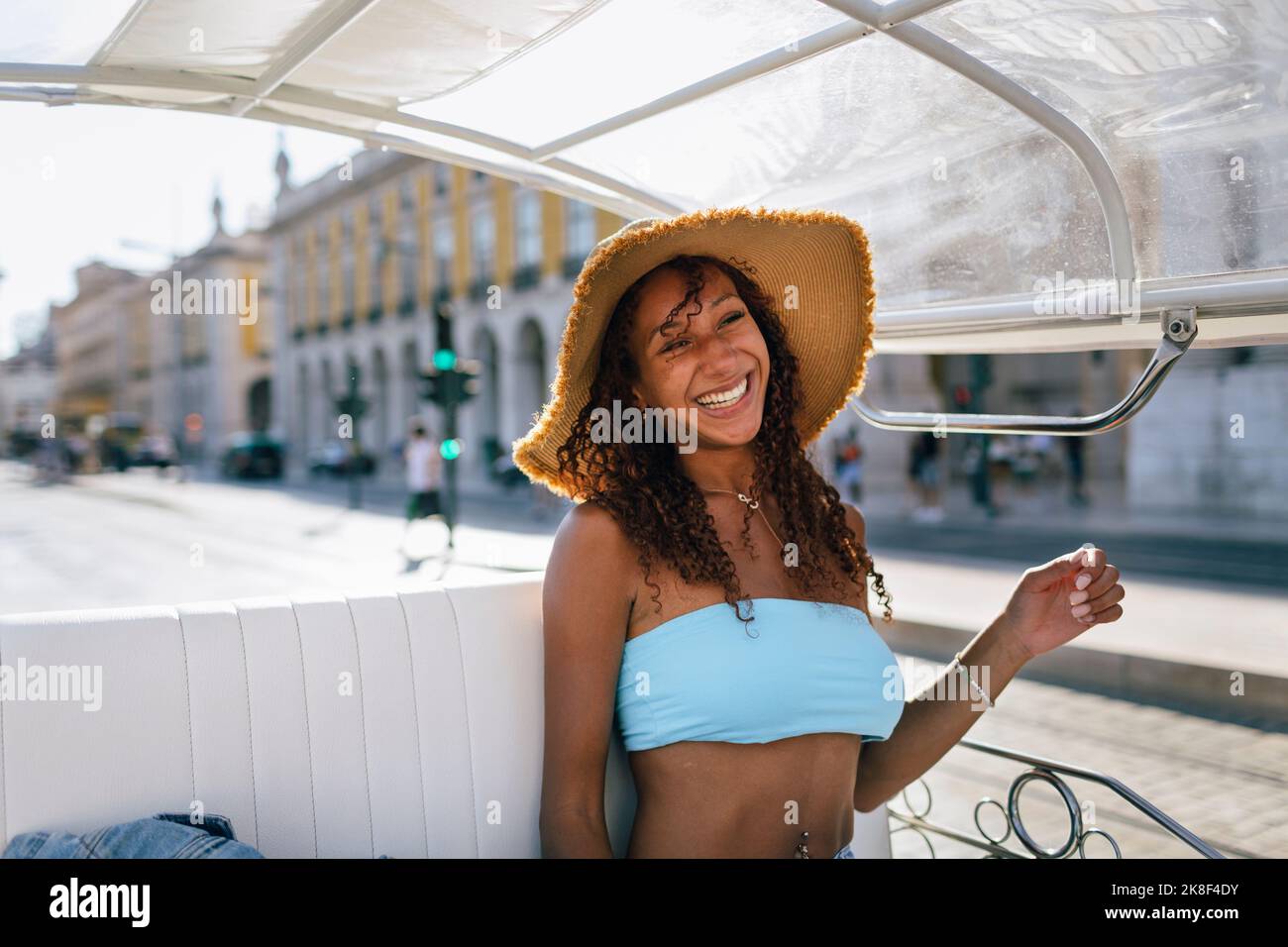Fröhliche junge Frau mit Hut, die an sonnigen Tagen Tuk Tuk Ride nimmt Stockfoto