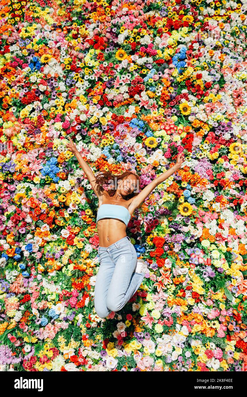Glückliche junge Frau, die vor einer bunten Blumenwand springt Stockfoto