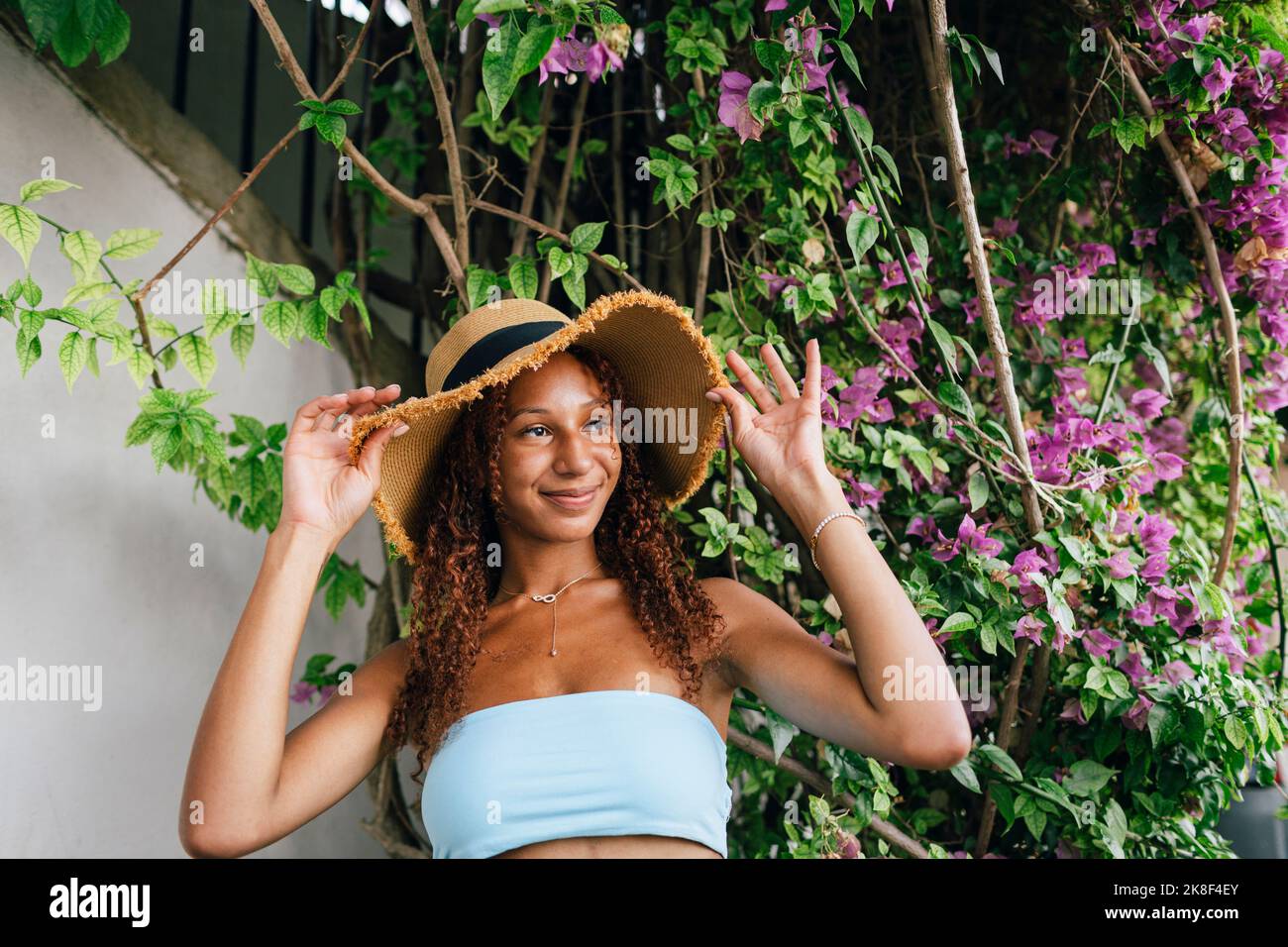 Lächelnde junge Frau mit Hut vor der Pflanze Stockfoto