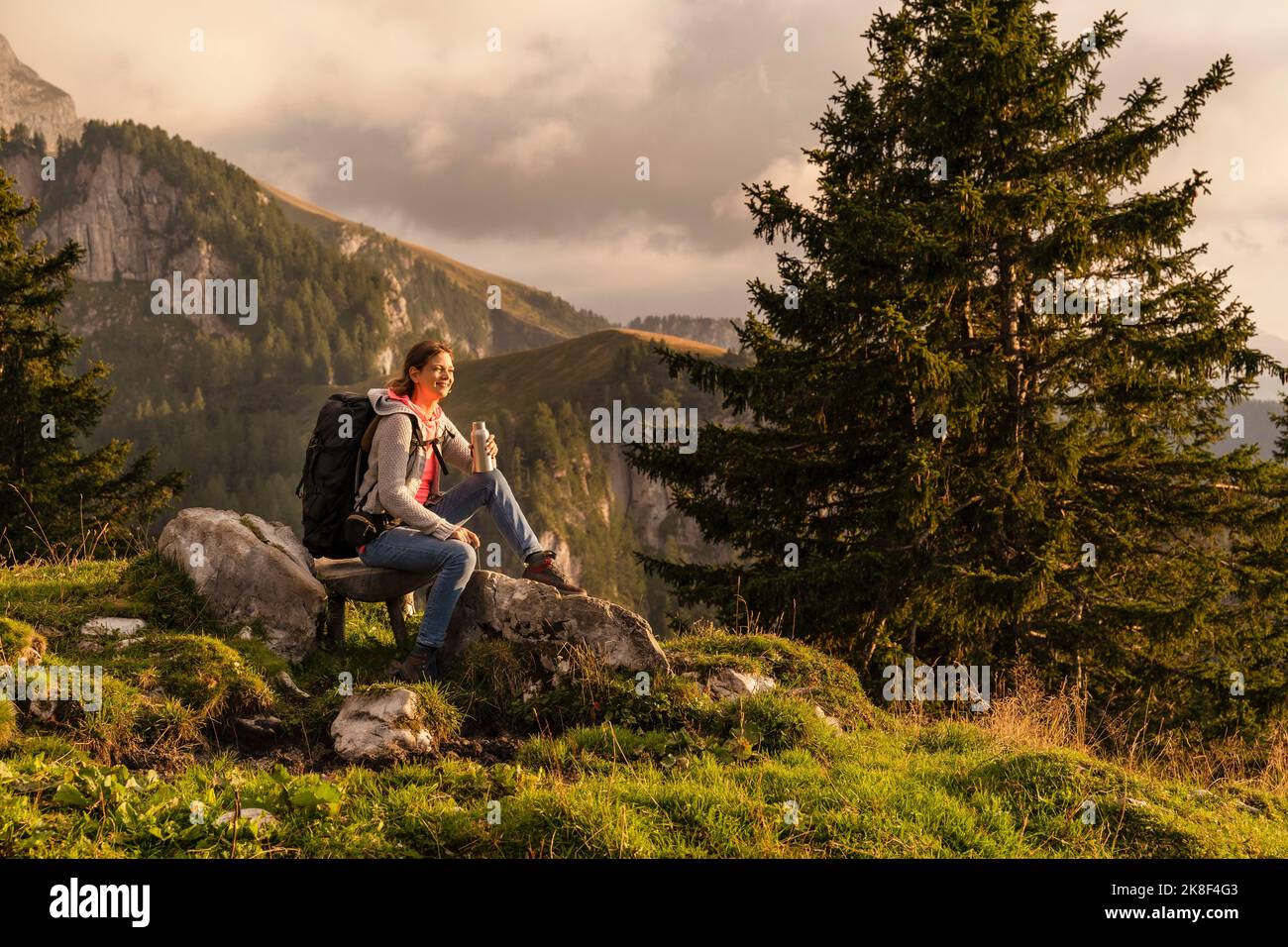 Lächelnde reife Frau mit Wasserflasche auf Felsen sitzend Stockfoto