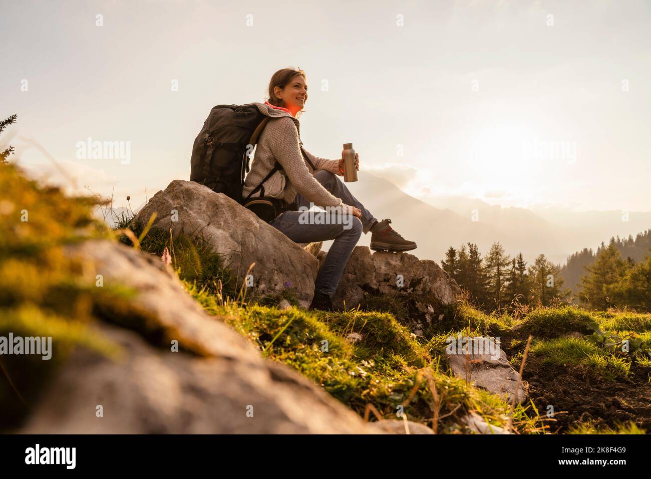 Lächelnde Frau mit Wasserflasche auf Felsen sitzend Stockfoto