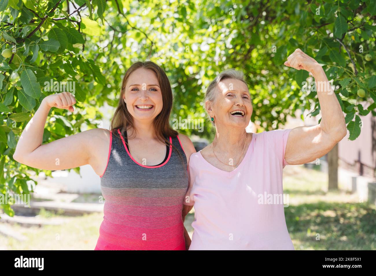 Aktive ältere Frau, die Muskeln anbiegend, mit einem Fitnesstrainer im Park Stockfoto