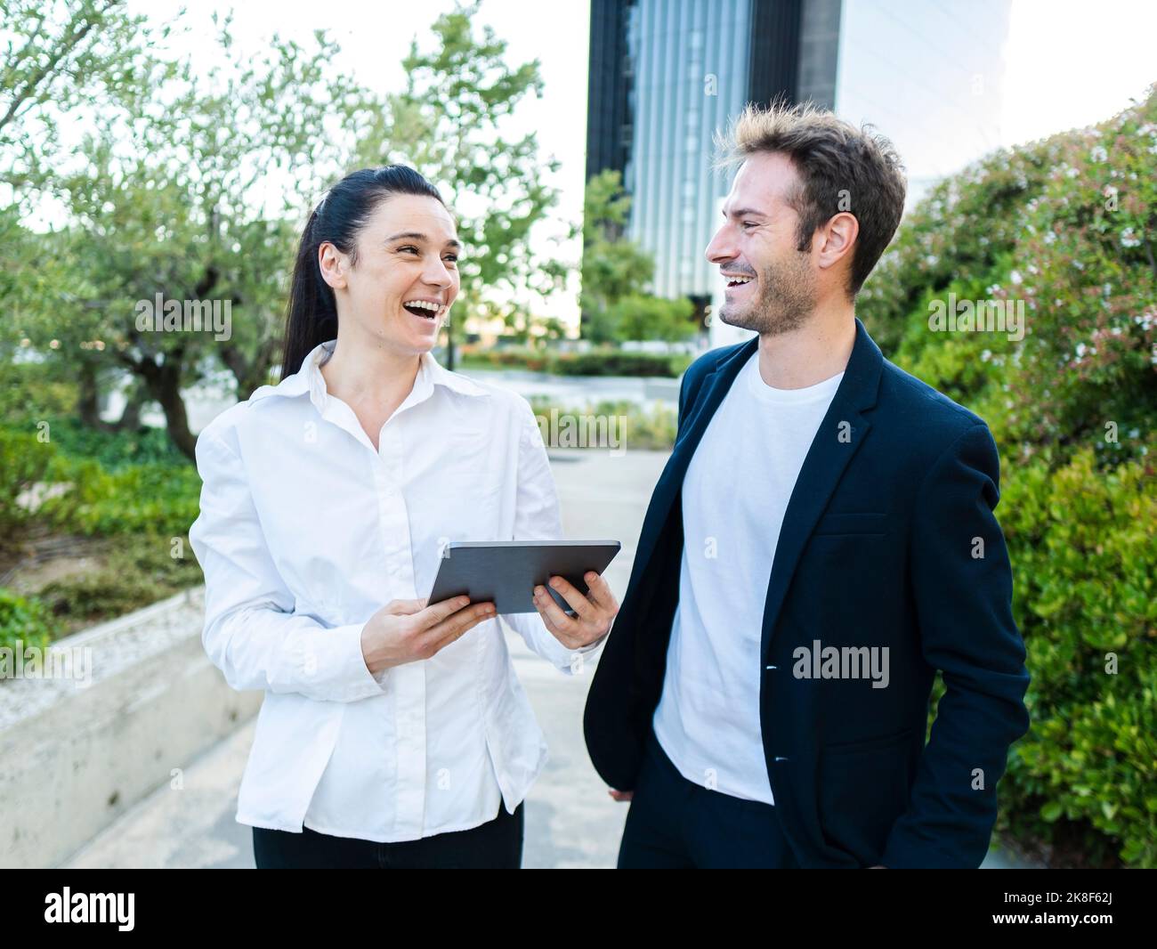 Fröhlicher Geschäftsmann mit Kollegen, der einen Tablet-PC im Büropark hält Stockfoto