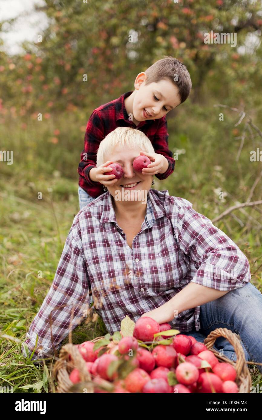 Verspielter Junge, der auf dem Bauernhof Äpfel über die Augen der Großmütter hält Stockfoto