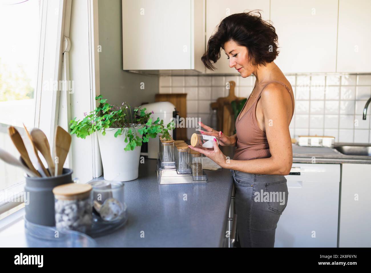 Frau, die einen Becher beschriftend an der Küchentheke ansah Stockfoto
