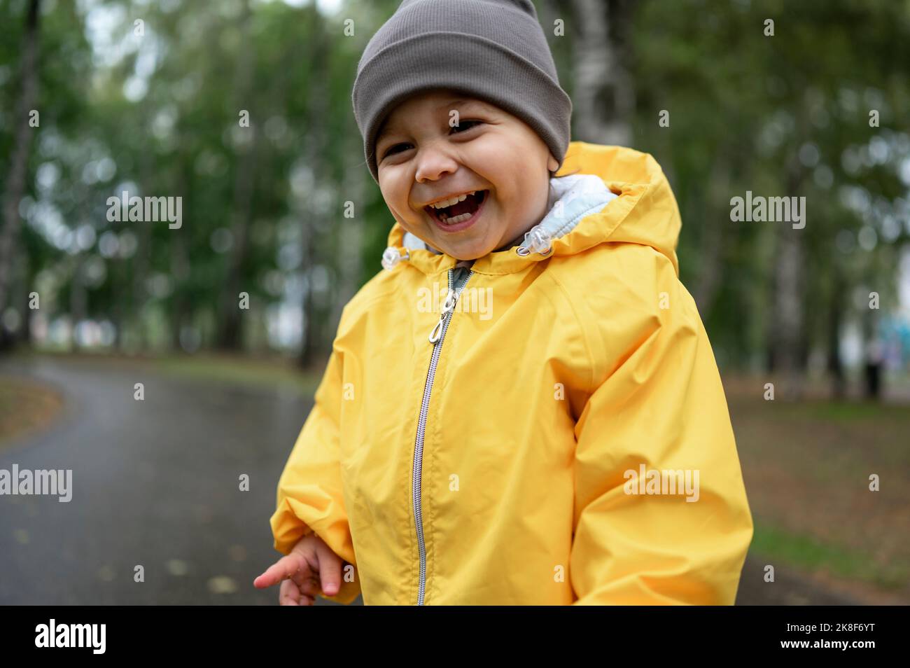 Netter fröhlicher Junge mit Strickmütze und gelber Regenjacke Stockfoto