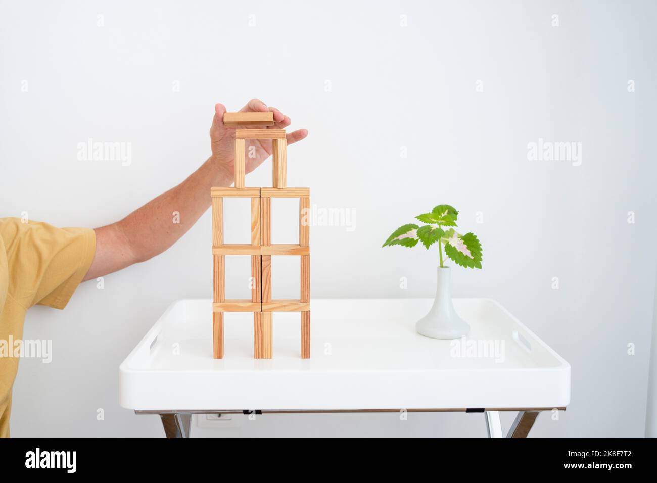 Hand des Mannes, der einen hölzernen Blockturm auf dem Tisch baut Stockfoto