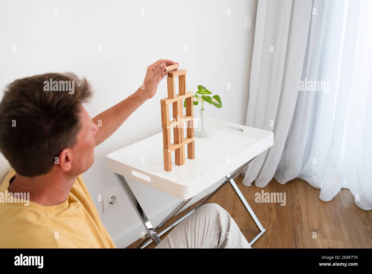 Reifer Mann, der zu Hause einen hölzernen Blockturm auf einem Couchtisch baut Stockfoto