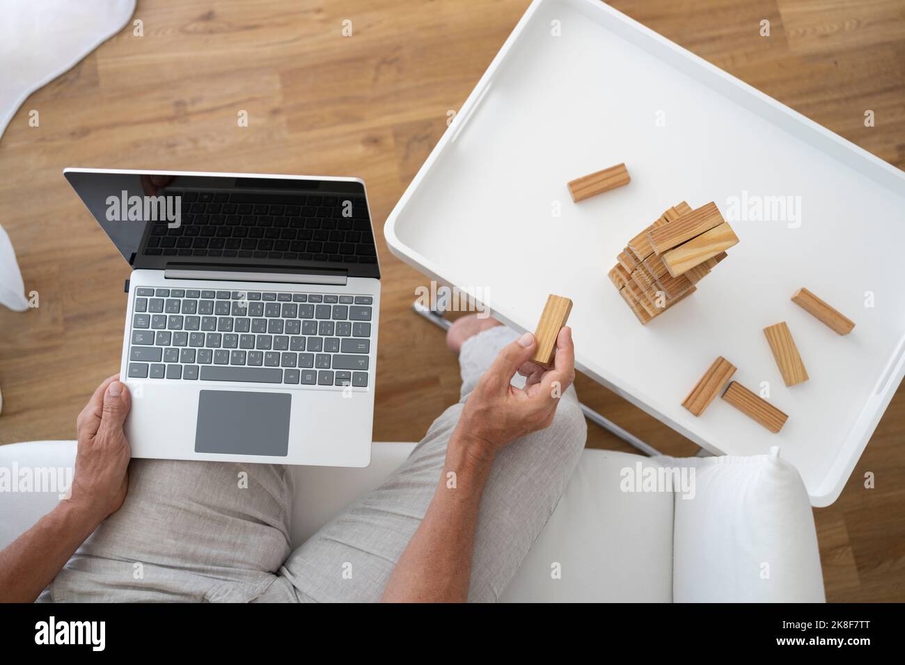 Hand eines reifen Mannes, der Laptop hält und zu Hause mit Spielzeugblöcken spielt Stockfoto