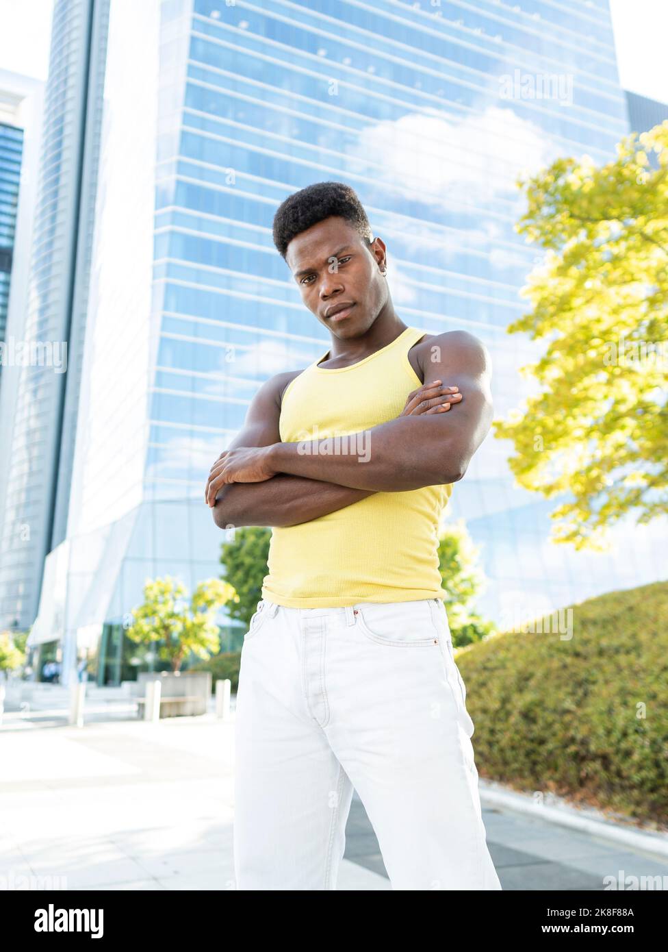 Junger Mann mit gelber Weste, der mit gekreuzten Armen vor dem modernen Gebäude steht Stockfoto