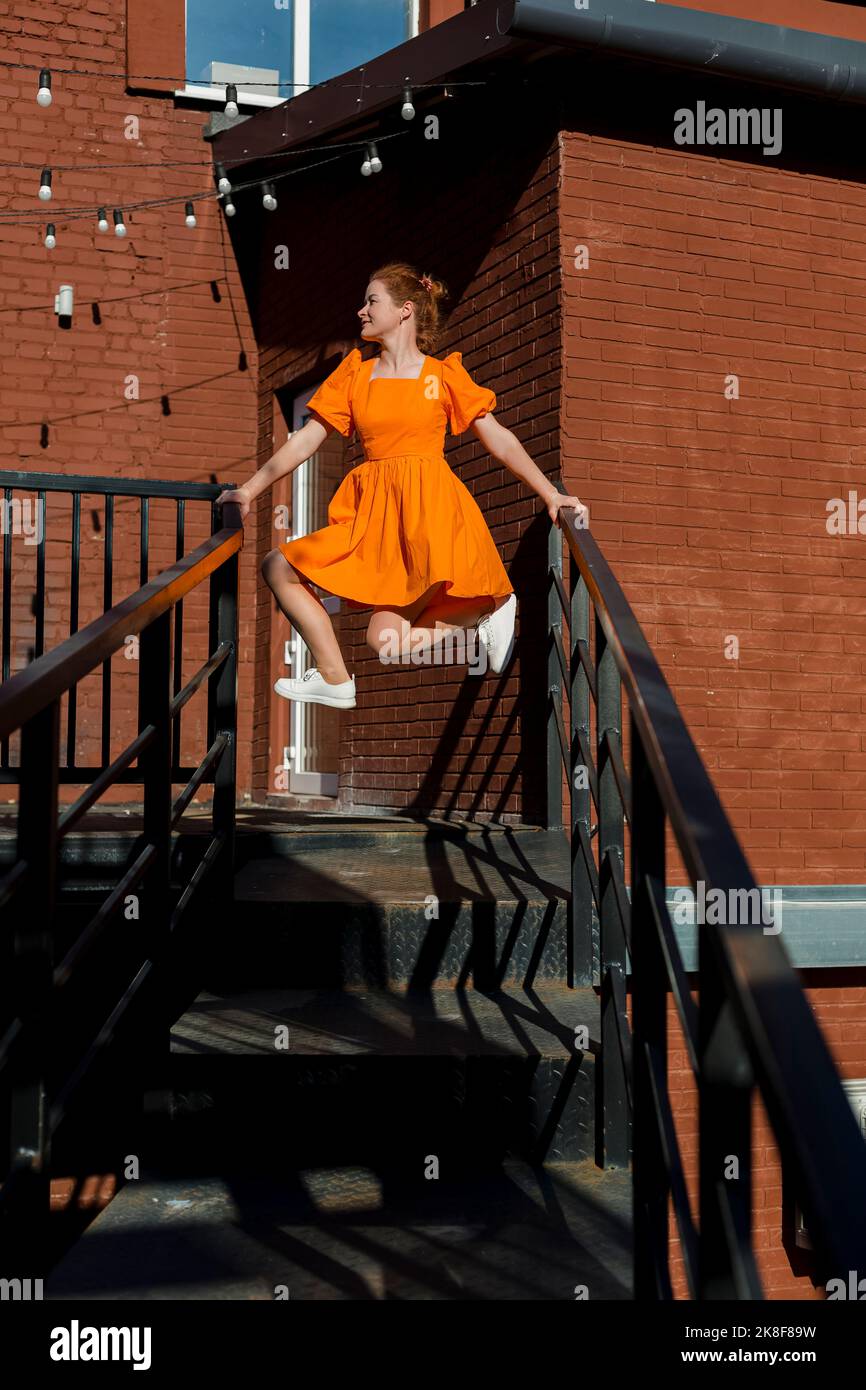 Frau in orangefarbenem Kleid, die auf dem Treppengeländer balanciert Stockfoto