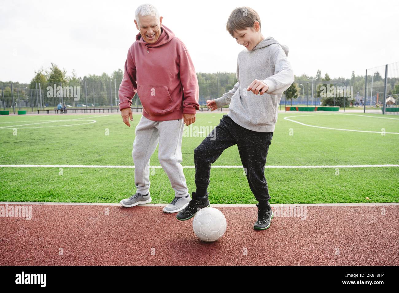 Glücklicher Junge mit Großvater, der auf dem Sportplatz mit Fußball spielt Stockfoto