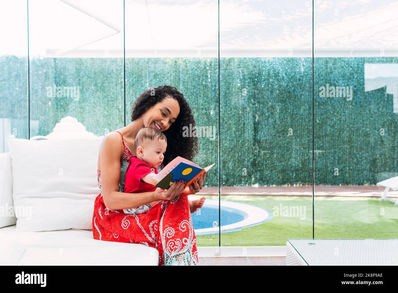 Glückliche Frau und Baby mit Bilderbuch sitzen auf dem Sofa zu Hause Stockfoto