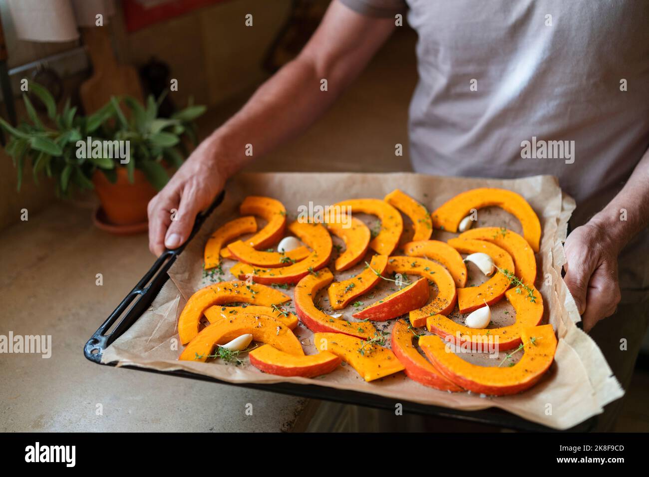 Hände eines Mannes, der Kürbisscheiben mit Thymian und Knoblauch in der Küche zeigt Stockfoto