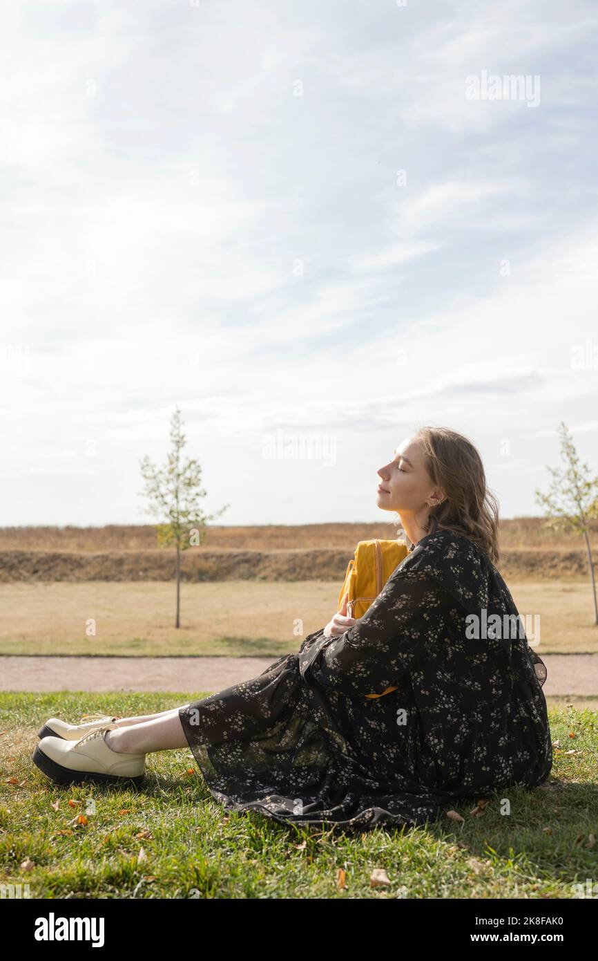 Junge Frau, die im Park bei Sonnenschein sitzt Stockfoto