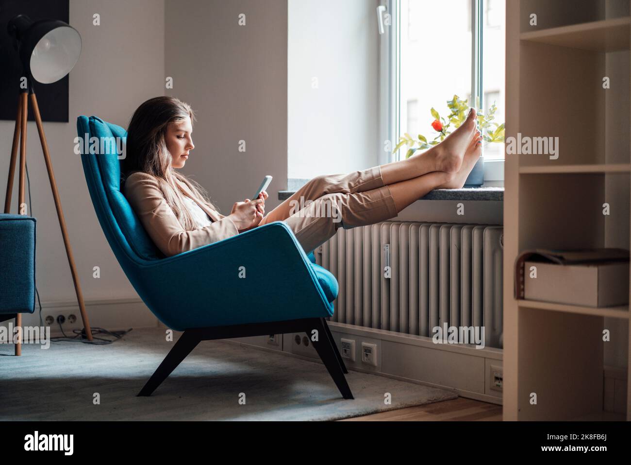 Geschäftsfrau mit den Füßen nach oben mit Smartphone auf dem Stuhl zu Hause Stockfoto