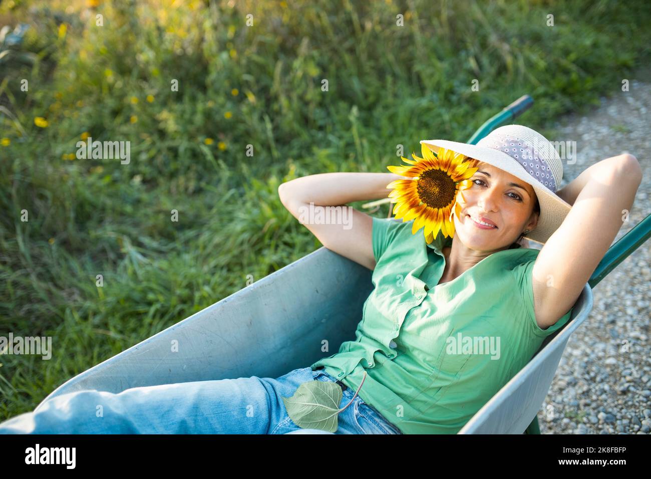 Lächelnder Gärtner mit Sonnenblume in Schubkarre liegend Stockfoto