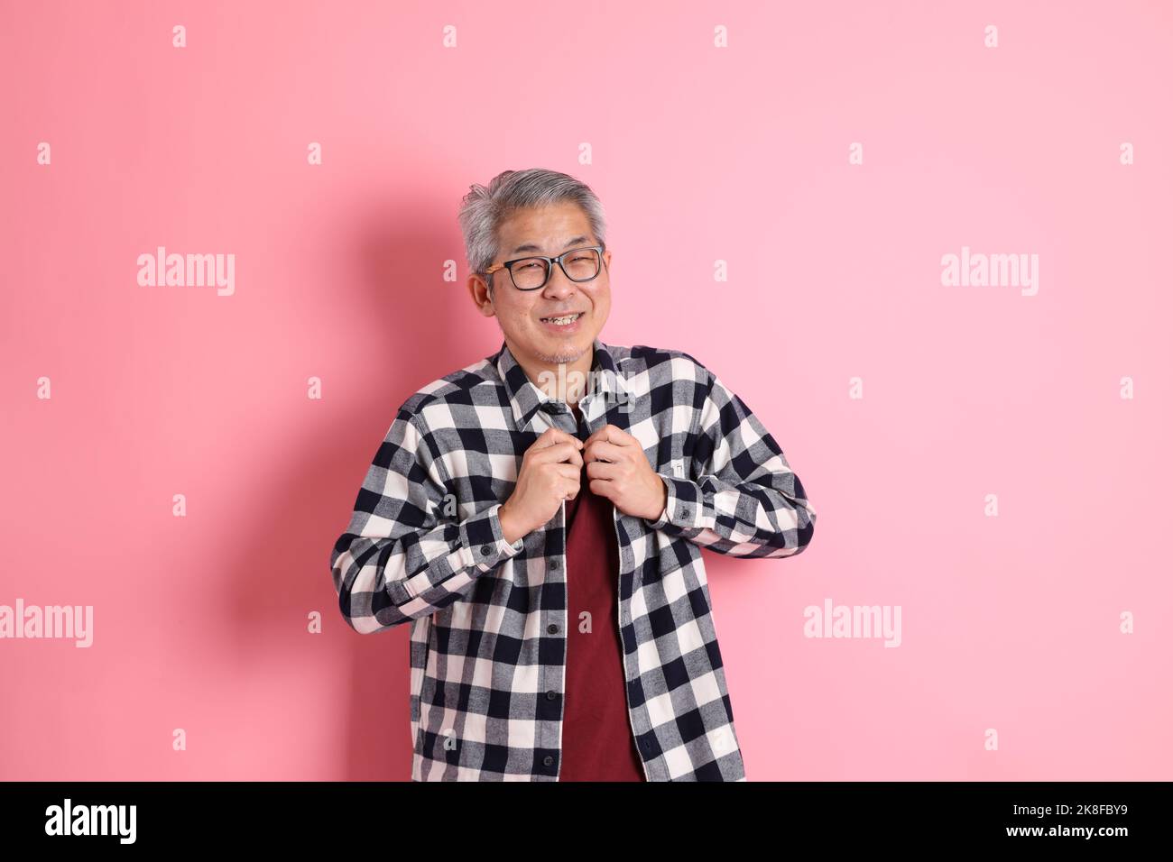 Der 40s-jährige asiatische Mann, der auf dem rosa Hintergrund mit legerer Kleidung stadiert. Stockfoto