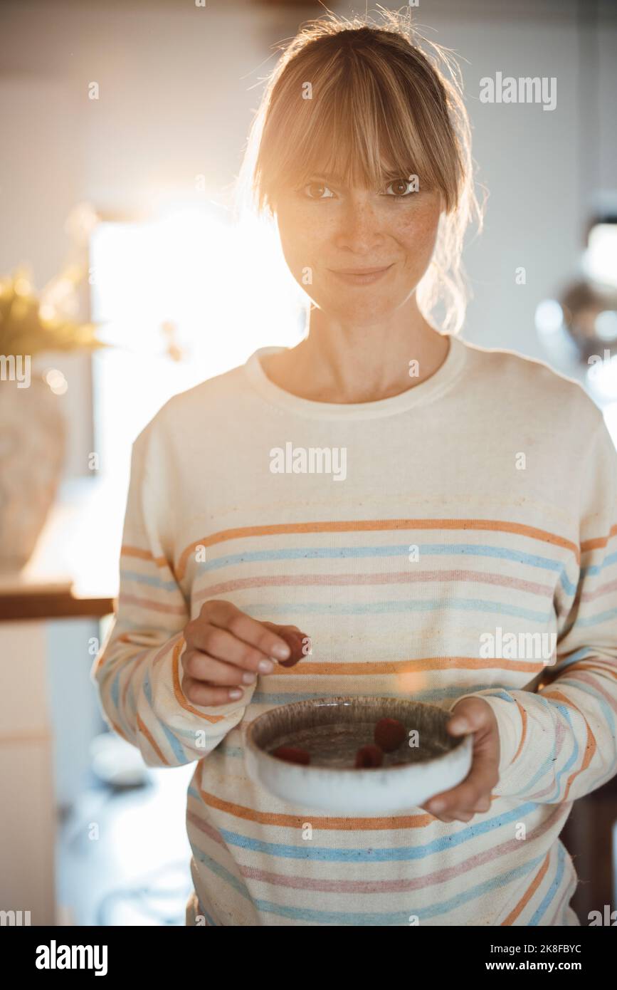 Lächelnde, schwanger Frau, die zu Hause Beeren auf dem Teller isst Stockfoto