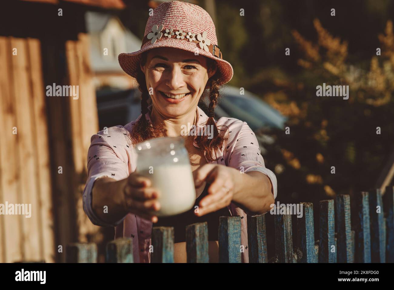 Lächelnde reife Frau, die am Zaun ein Glas mit frischer Milch gibt Stockfoto