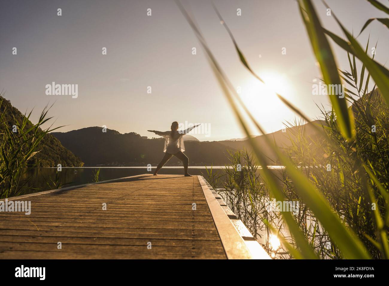 Reife Frau übt Kriegerpose auf dem Steg am See Stockfoto