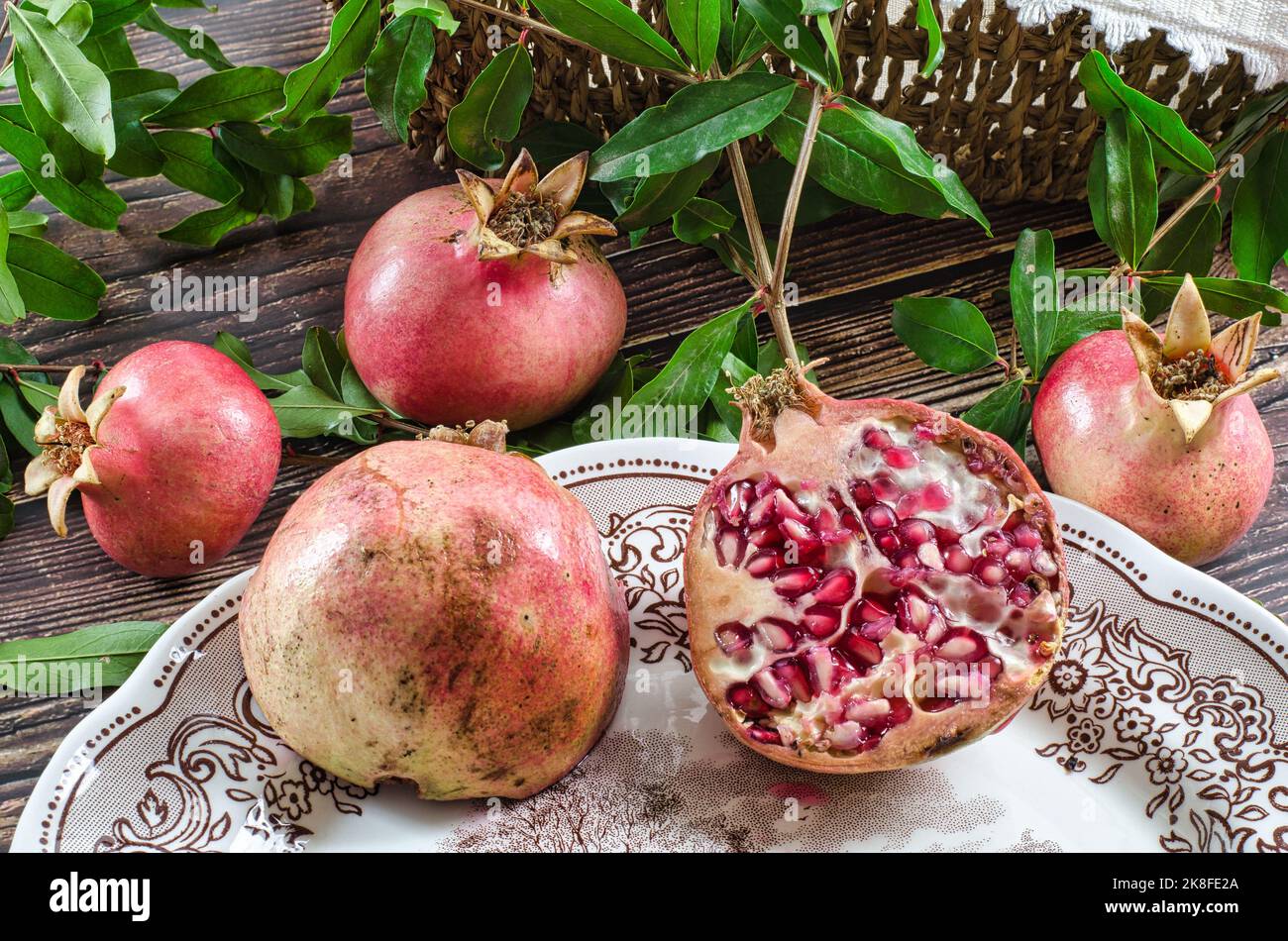 Gruppe von Granatäpfeln auf einem rustikalen Holztisch. Ein Granatapfel, der in zwei Teile innerhalb eines Vintage-Tellers geschnitten wurde Stockfoto