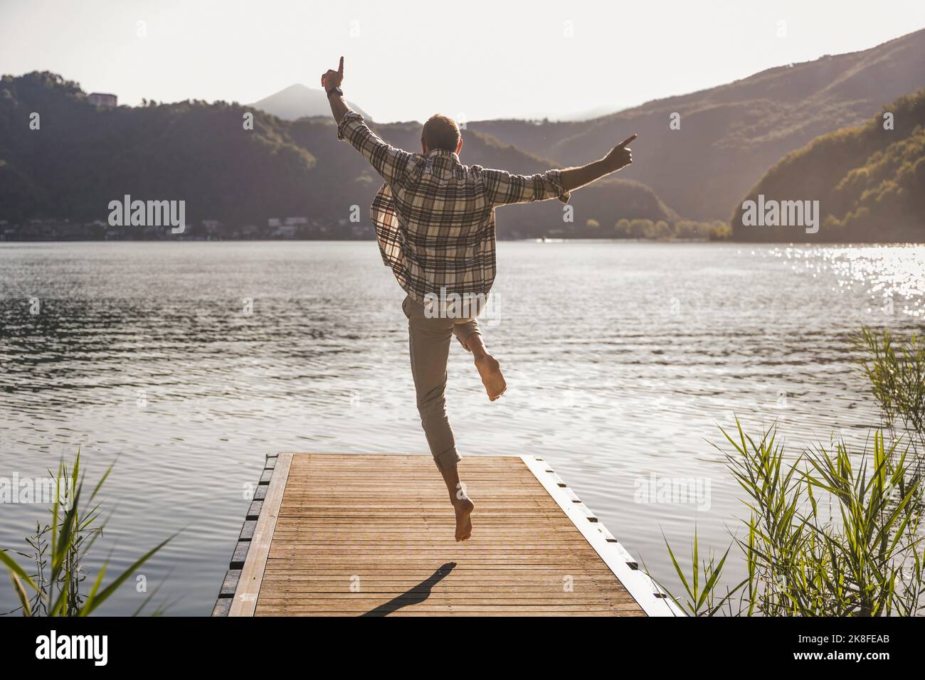 Reifer Mann, der im Urlaub auf dem Steg über den See springt Stockfoto