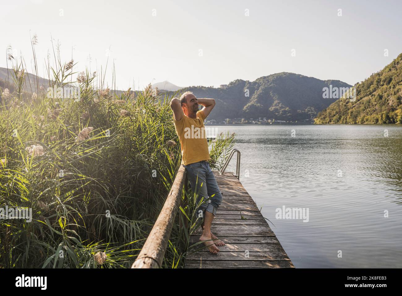 Reifer Mann mit den Händen hinter dem Kopf auf dem Steg am See im Urlaub Stockfoto