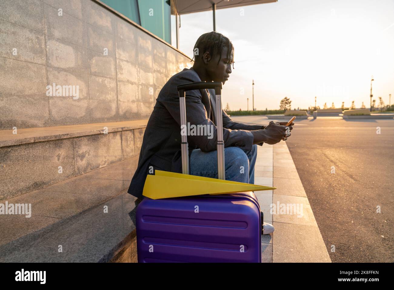 Geschäftsmann mit Smartphone mit Koffer und Papierflugzeug auf Treppen Stockfoto