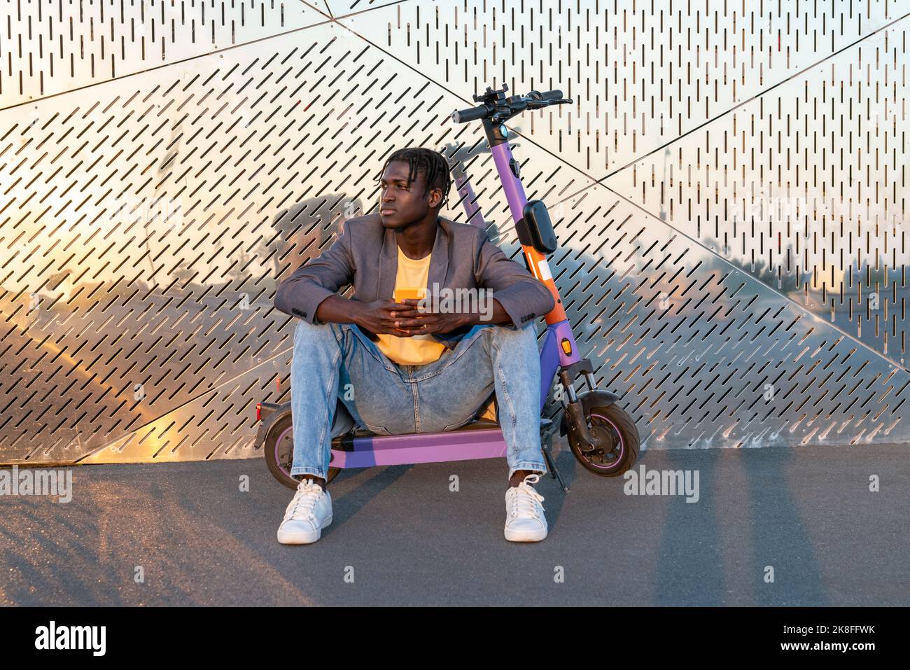 Geschäftsmann hält Smartphone auf Elektro-Roller vor der Metallwand Stockfoto