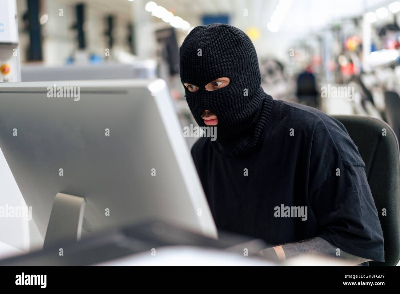 Computerhacker tragen Maske mit Desktop-PC im Lager Stockfoto