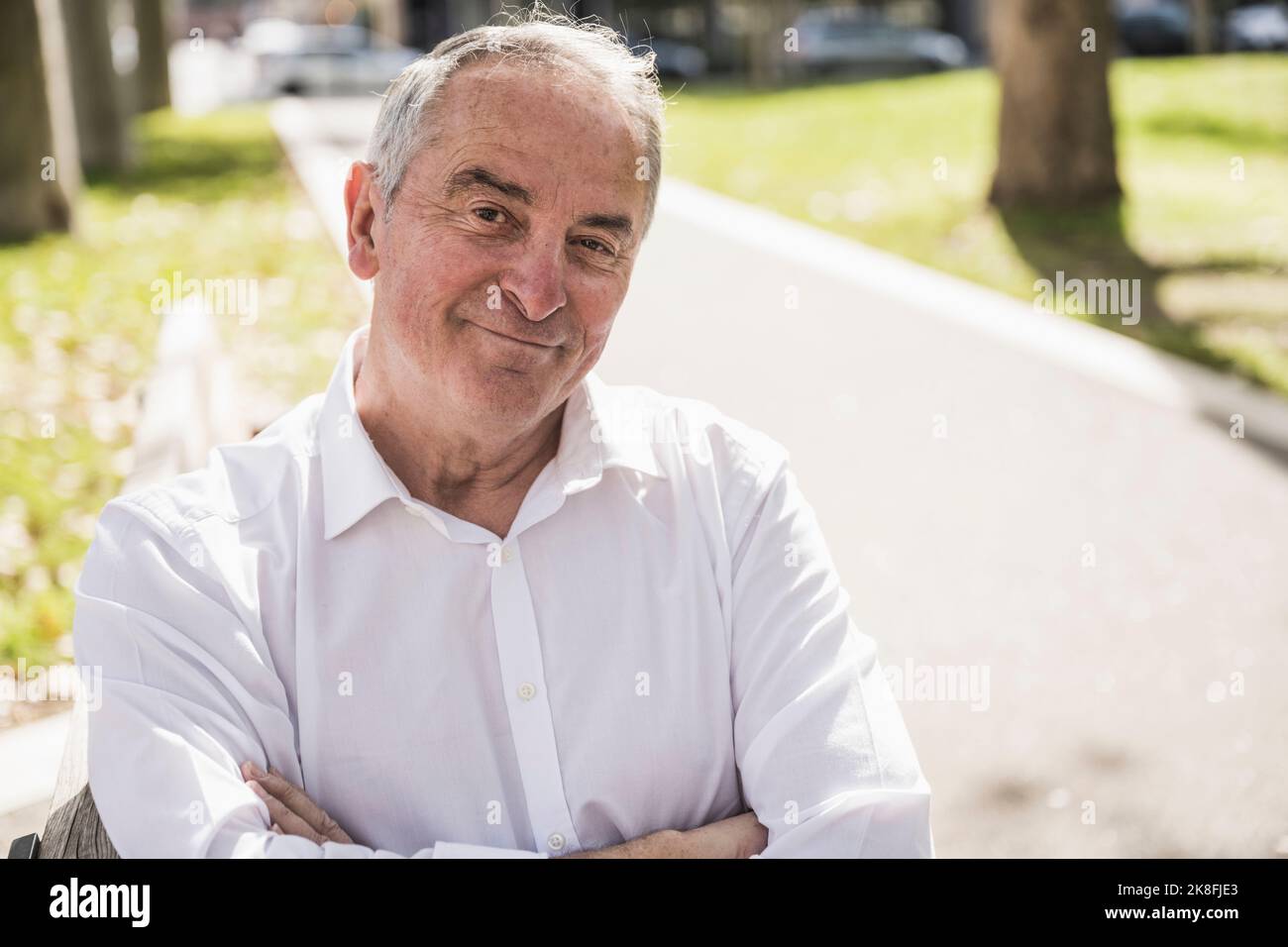 Lächelnder älterer Mann mit gekreuzten Armen an einem sonnigen Tag Stockfoto