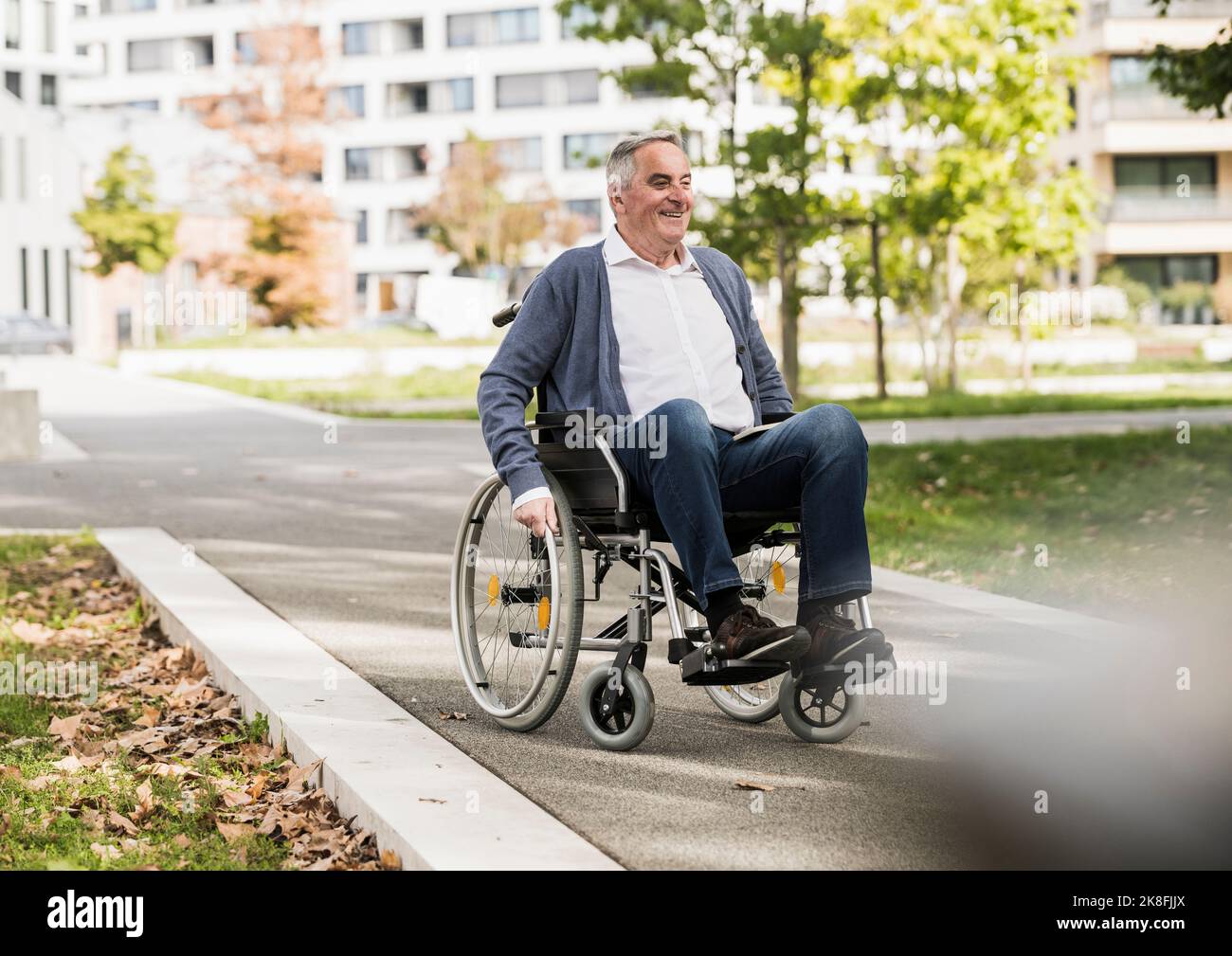 Lächelnder älterer Mann im Pullover, der auf dem Rollstuhl sitzt Stockfoto