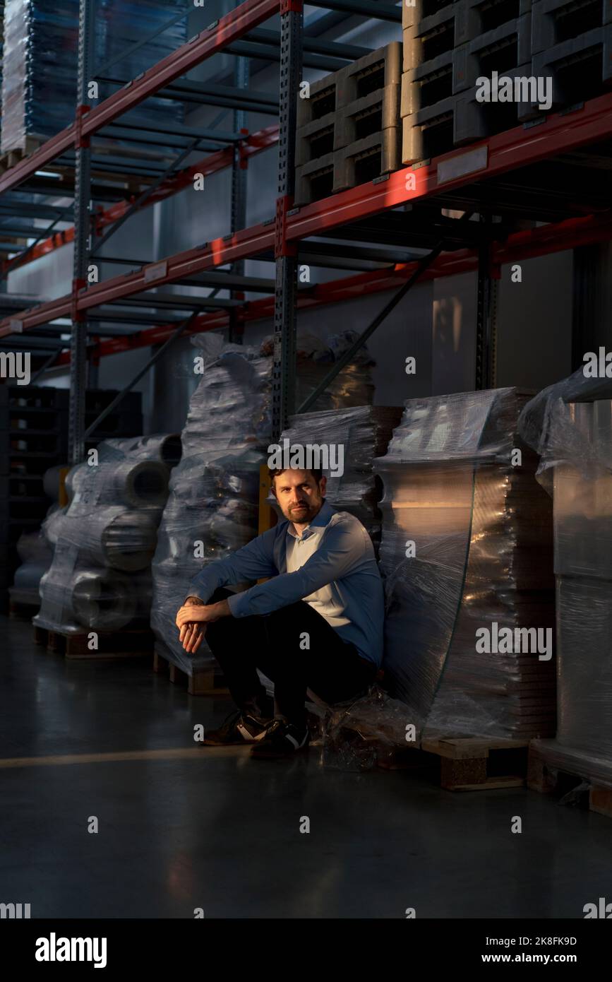Geschäftsmann, der im Lagerhaus an einem Regal hocken wird Stockfoto
