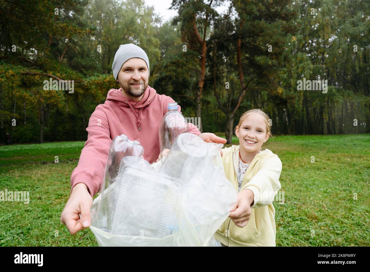 Lächelnder Mann mit Tochter, der im Wald gesammelten Plastikmüll zeigt Stockfoto