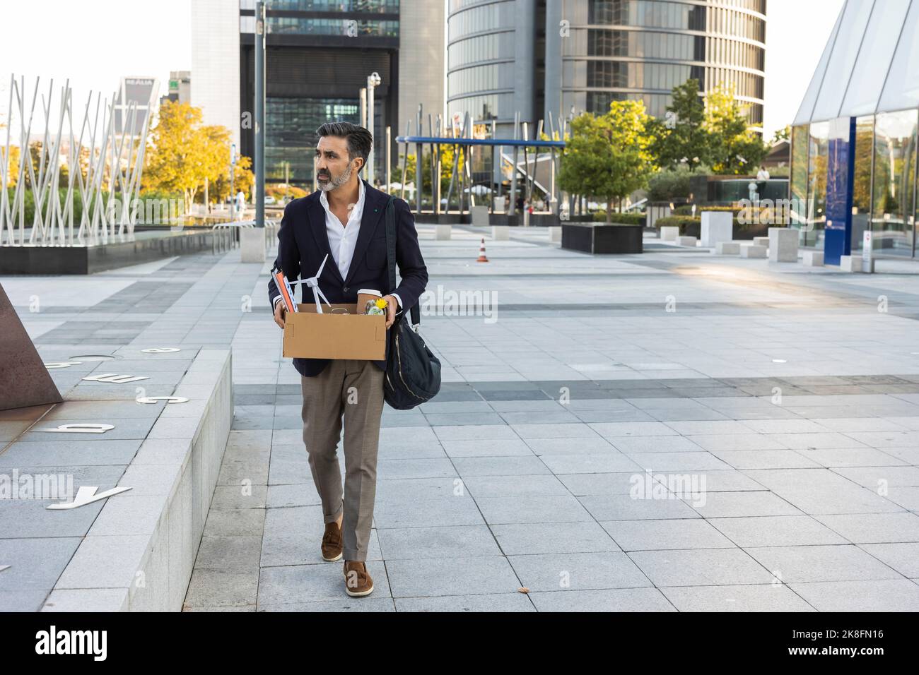 Ein Geschäftsmann hält einen Kasten in der Hand, der vor dem Bürogebäude läuft Stockfoto