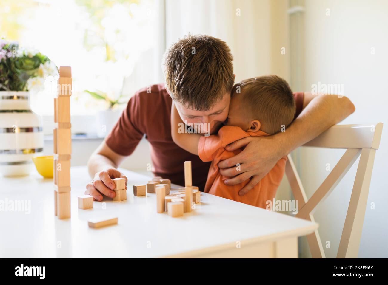 Sohn umarmt Vater durch gestapelte Spielzeugblöcke auf dem Tisch zu Hause Stockfoto