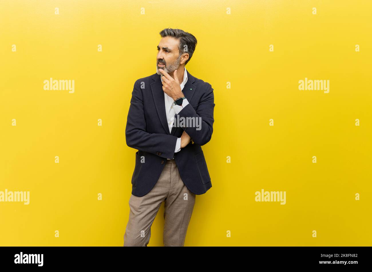 Nachdenklicher Geschäftsmann mit der Hand am Kinn, der gegen die gelbe Wand steht Stockfoto