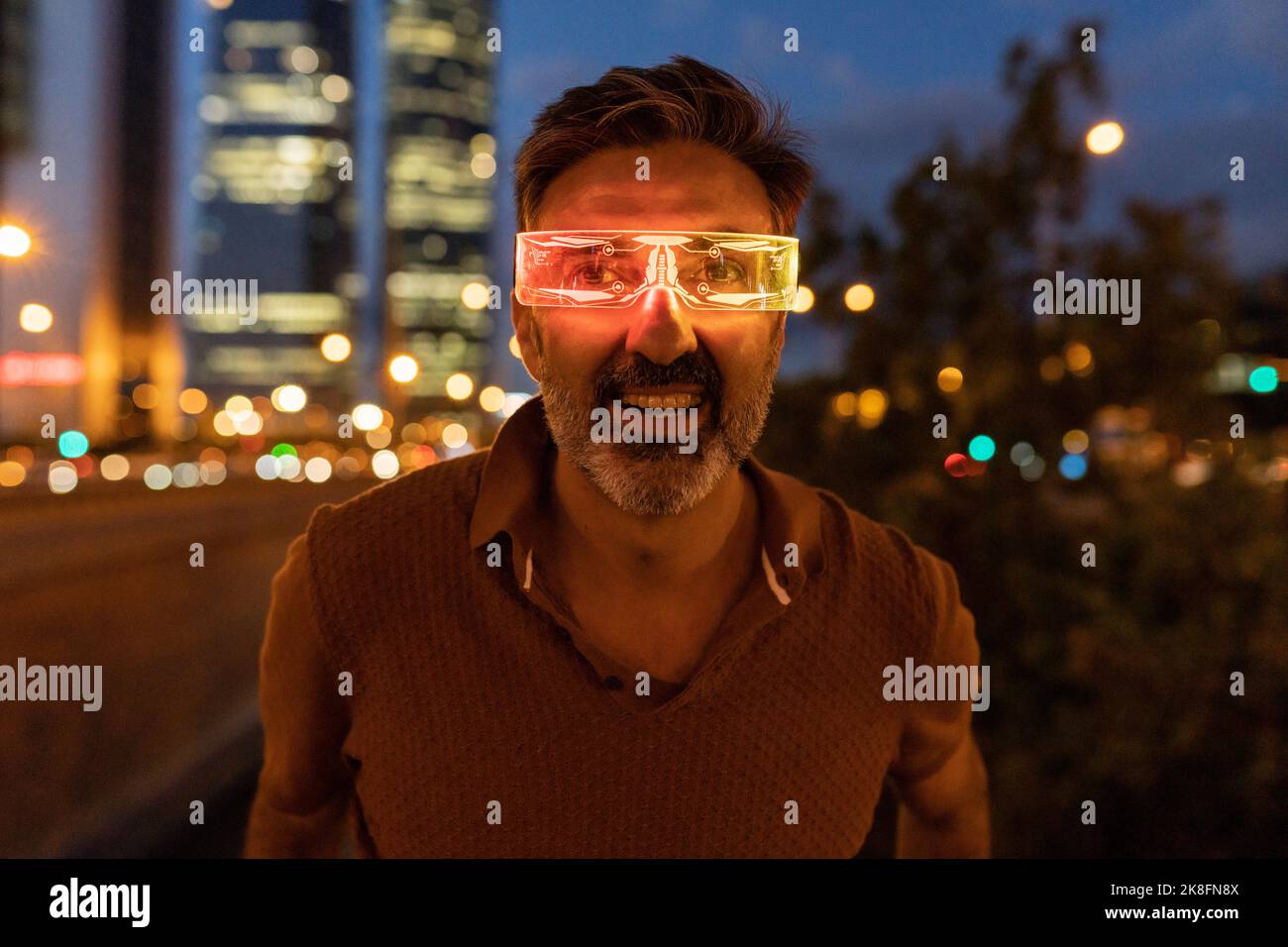 Ein glücklicher Geschäftsmann, der nachts eine beleuchtete Smart-Brille trägt Stockfoto