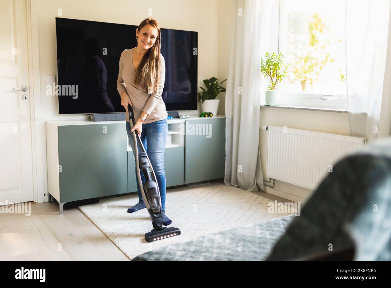 Lächelnde Frau, die zu Hause den Staubsauger auf dem Teppich verwendet Stockfoto