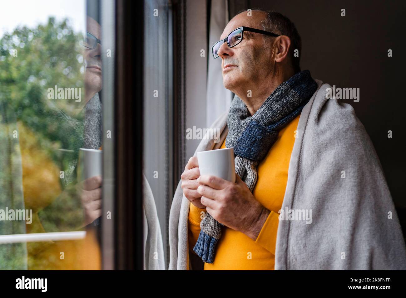 Nachdenklicher Mann mit Tee und Blick aus dem Fenster zu Hause Stockfoto