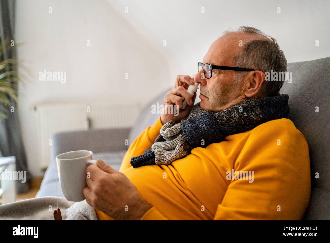 Älterer Mann mit Nasenspray sitzt zu Hause auf dem Sofa Stockfoto