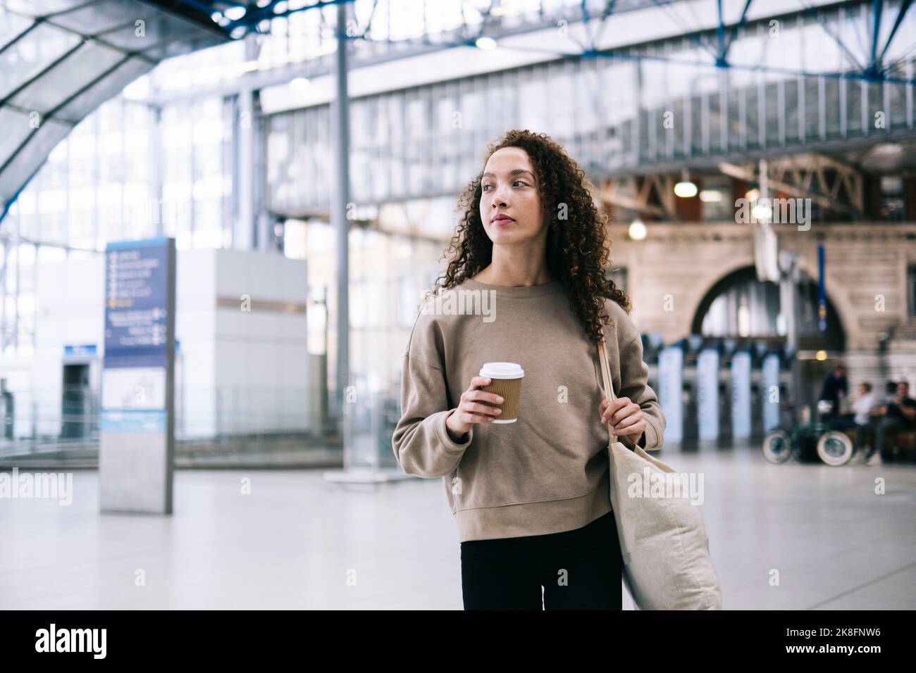 Junge Frau, die mit einer Tasse Kaffee zum Einwegnehmen am Bahnhof steht Stockfoto