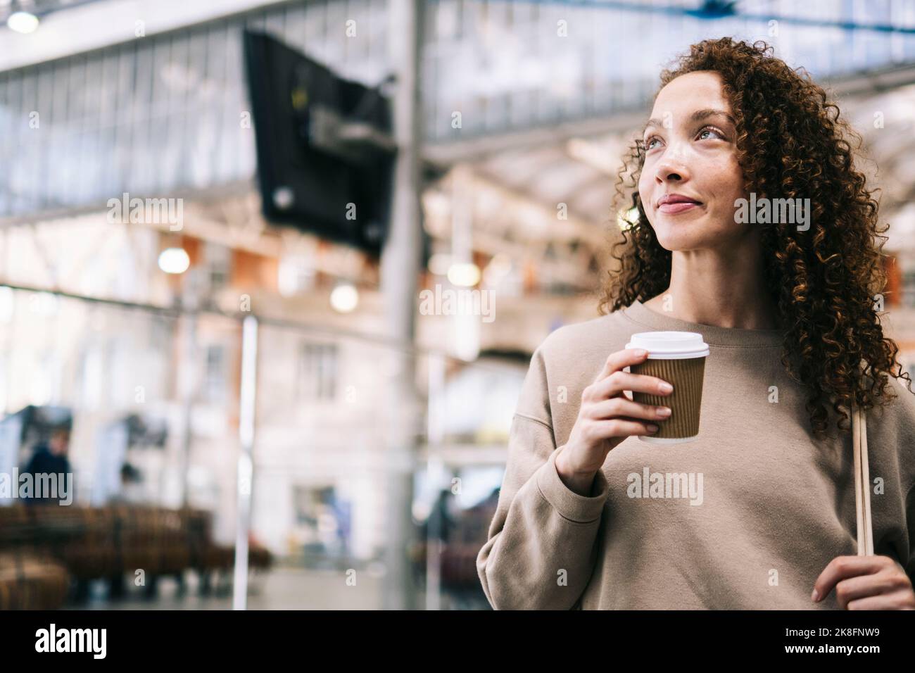 Lächelnde Frau mit einer Tasse Kaffee zum Einwegnehmen am Bahnhof Stockfoto