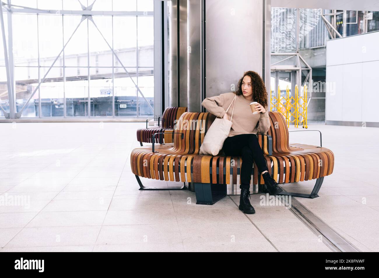 Junge Frau, die auf dem Sitz am Bahnhof sitzt Stockfoto