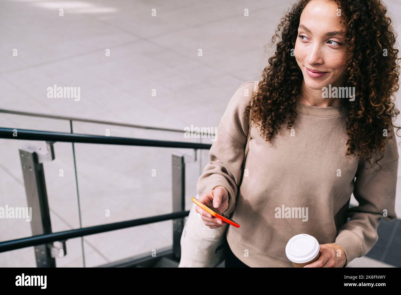 Lächelnde Frau mit Mobiltelefon, das sich auf der Treppe hochbewegt Stockfoto
